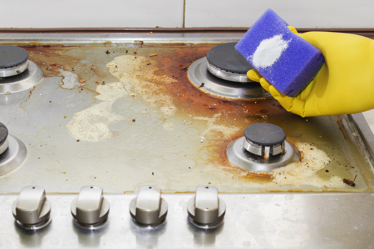 gloved hand uses sponge and cleaning powder to clean gas stove top