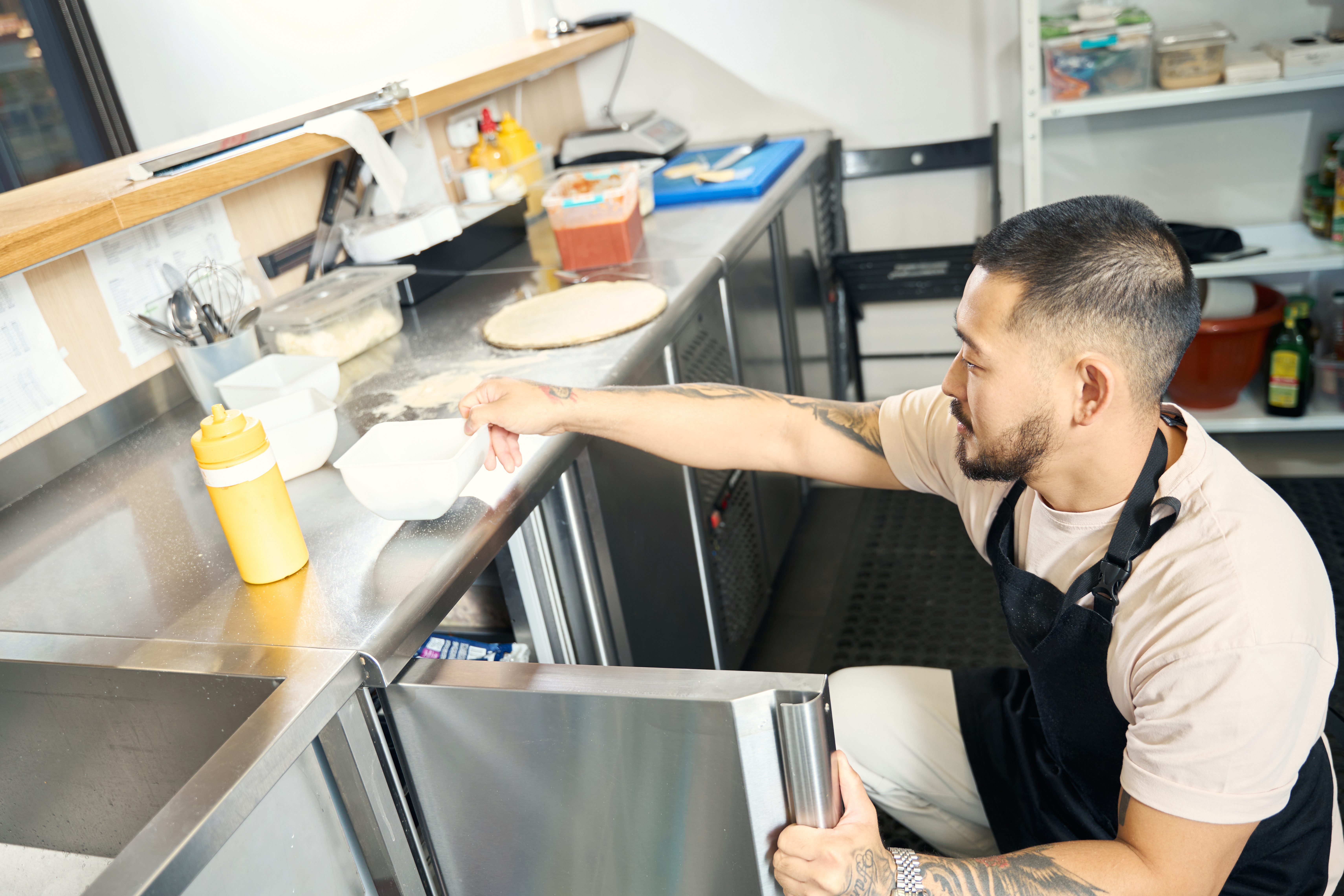 A young food worker searching for ingredients in a reach in refrigerator 