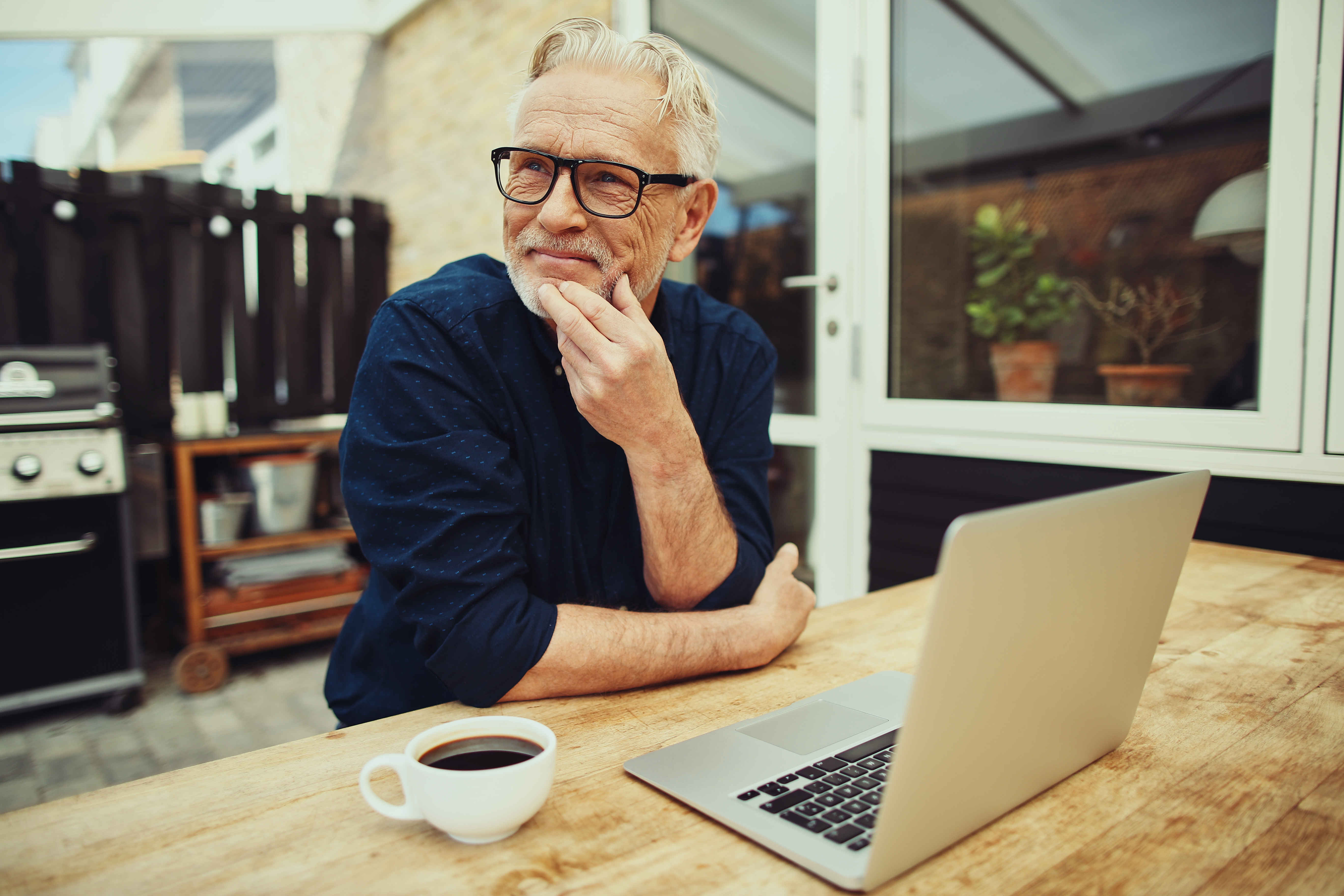 A middle-aged man in a backyard thinking with a cup of coffee and an open laptop 
