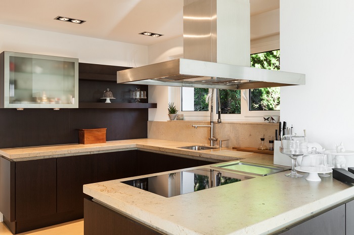 Interior of a modern, domestic kitchen with large island countertop and overhead island range hood. 
