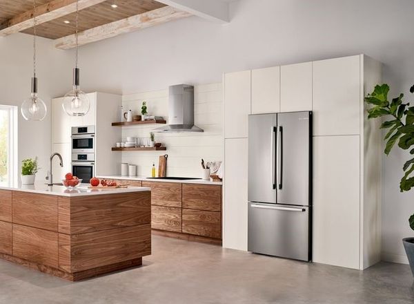 angled view of a white kitchen with wood grain cabinetry and a large french door built in refrigerator in the wall on the right
