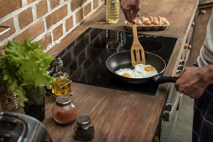 Young man preparing eggs for breakfast in kitchen at home on an induction cooktop. 