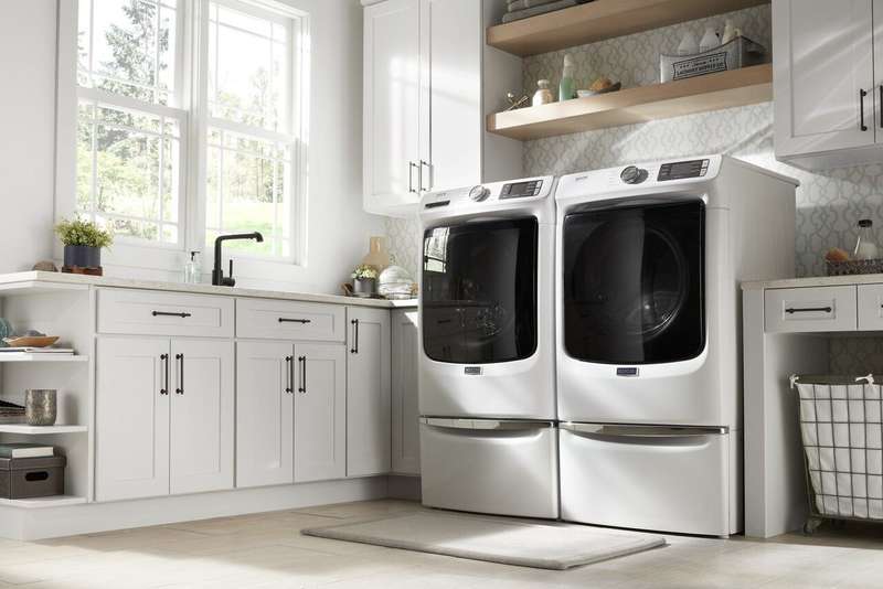 Modern laundry room with sink and natural light coming through the window with Maytag laundry appliances in the middle. 