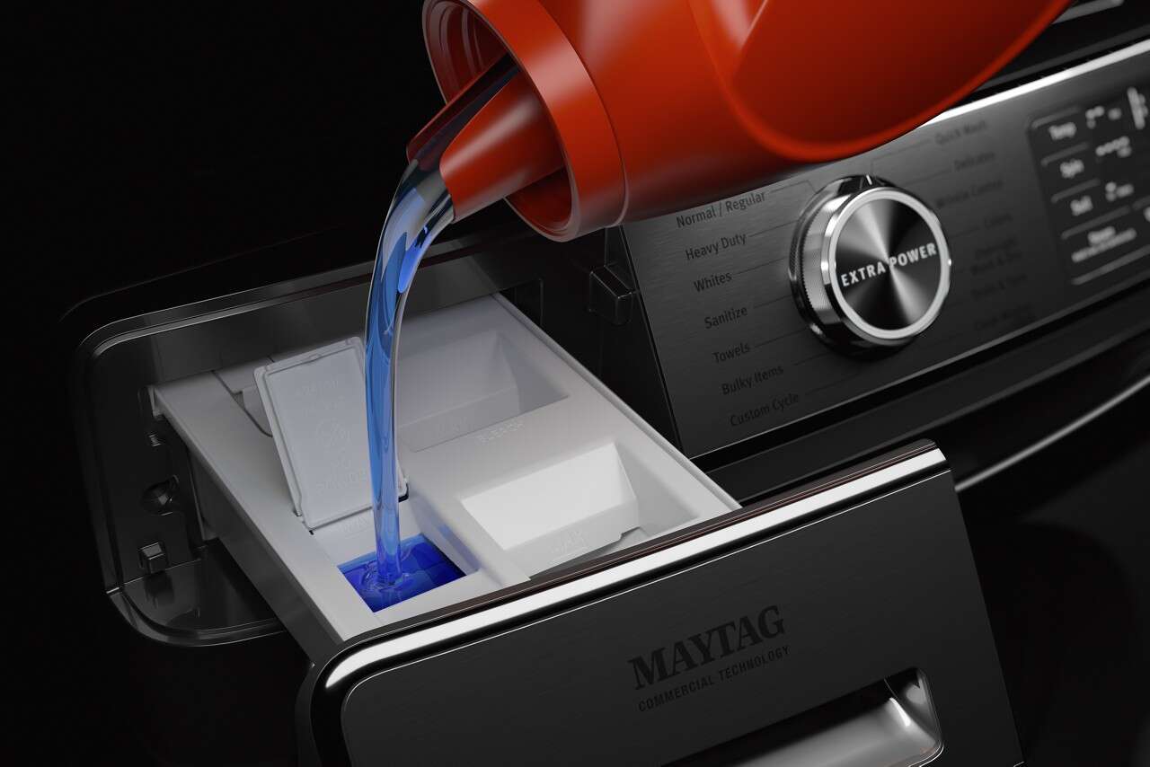 A user pouring detergent into the dispenser of a Maytag front load washer 
