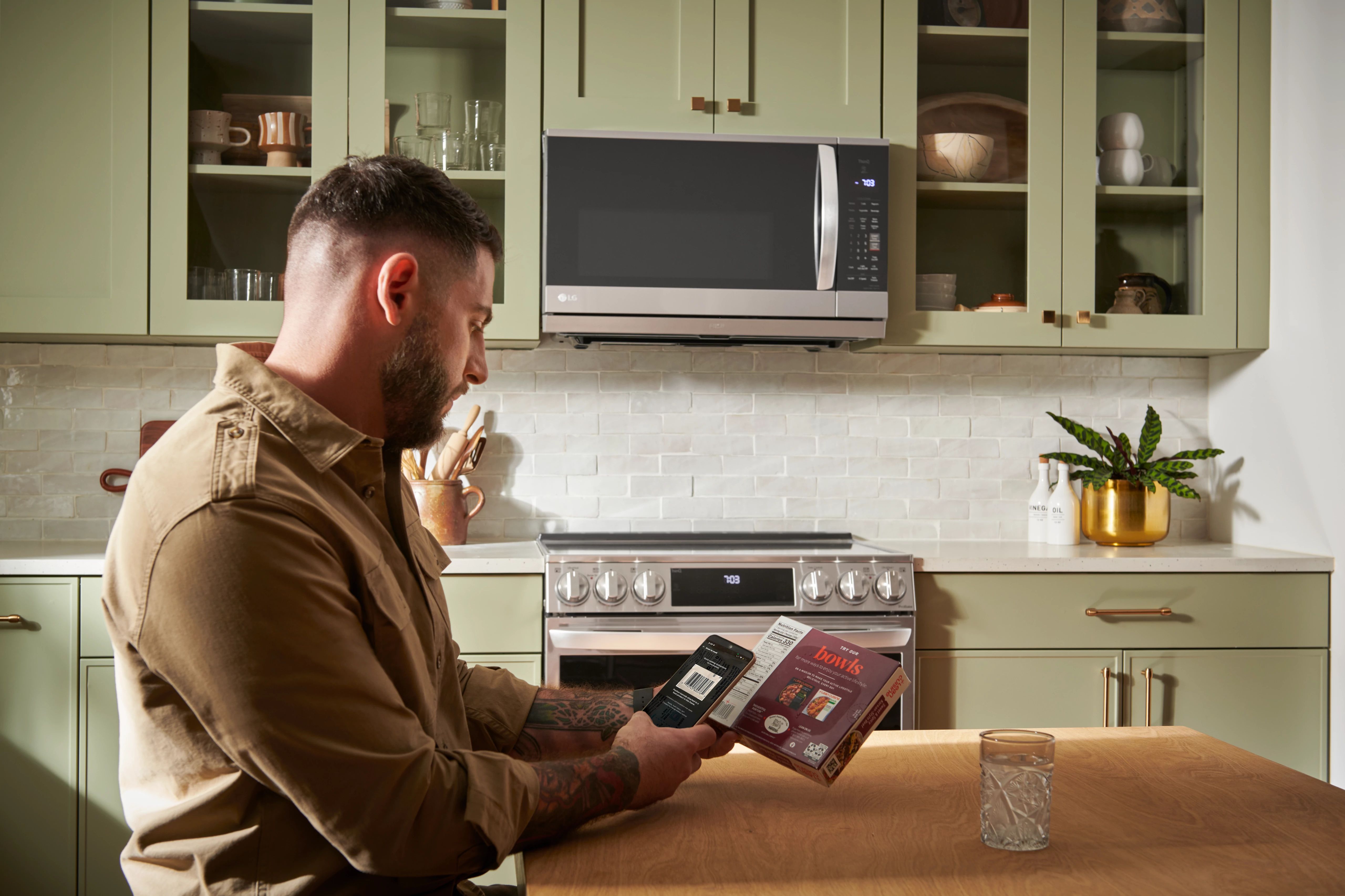 A man scanning the barcode of a frozen dinner in a kitchen featuring an LG range and over-the-range microwave 