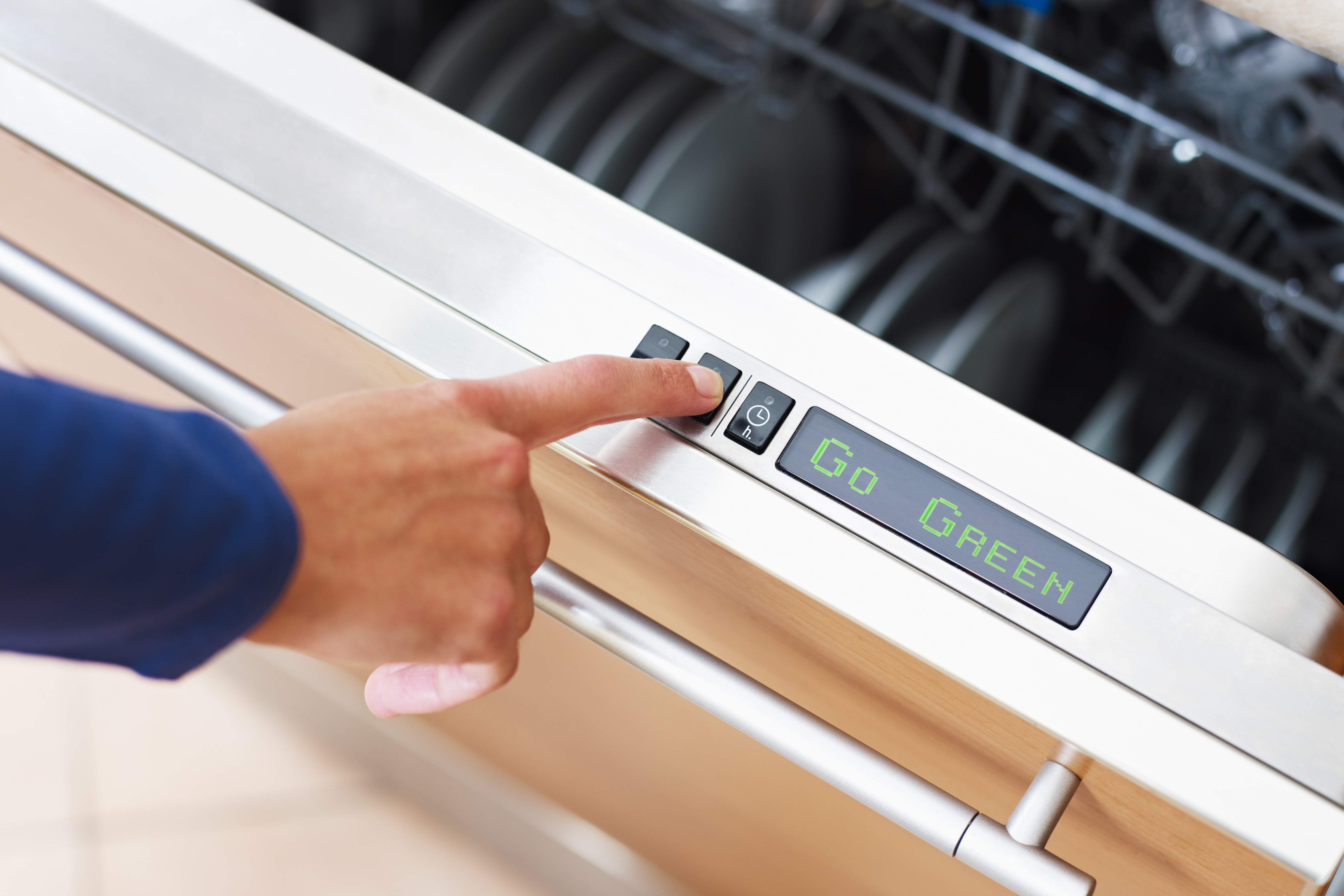 A person pressing a button on a dishwasher with the display saying Go Green 