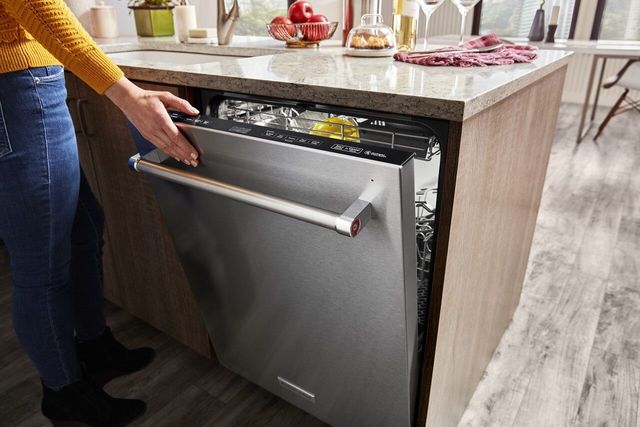view of a womans arm reaching into frame to close a built in dishwasher