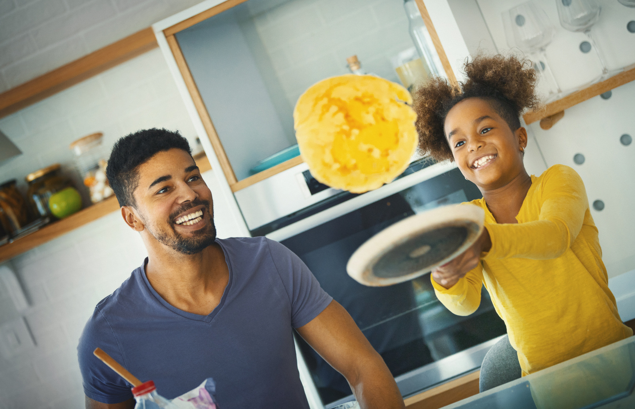 father and daughter have fun flipping pancakes over induction cooktop 