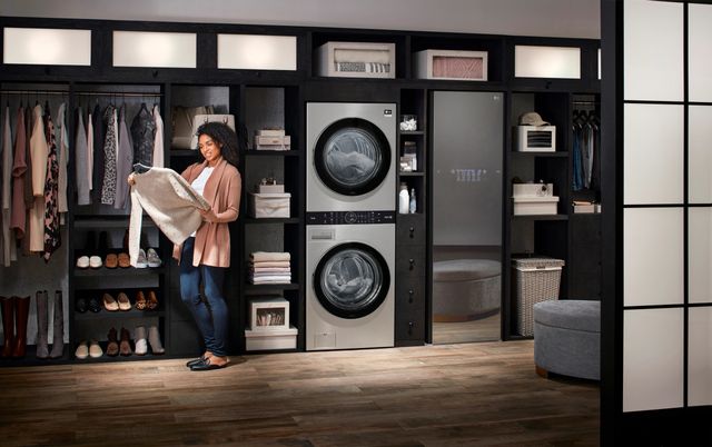 front view of a woman standing looking at a sweater next to a silver stackable laundry pair in a luxury laundry room
