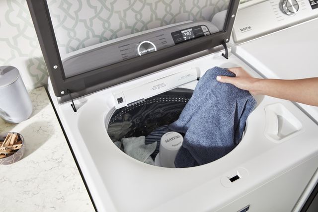top view of an arm putting a blue towel into a Maytah top load washer