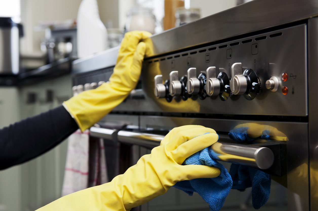 two hands cleaning a black oven range in a domestic kitchen