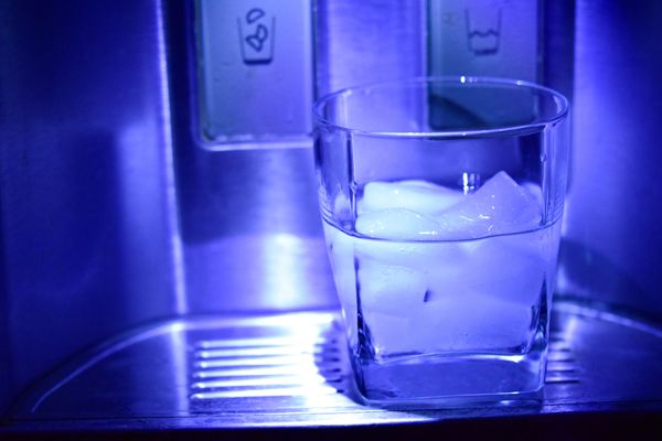 Clear drinking glass filled with water and ice, placed at the dispenser of a refrigerator