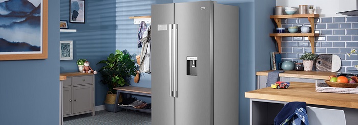 Photo of a modern kitchen painted blue with a stainless steel Beko counter depth refrigerator in the middle. 