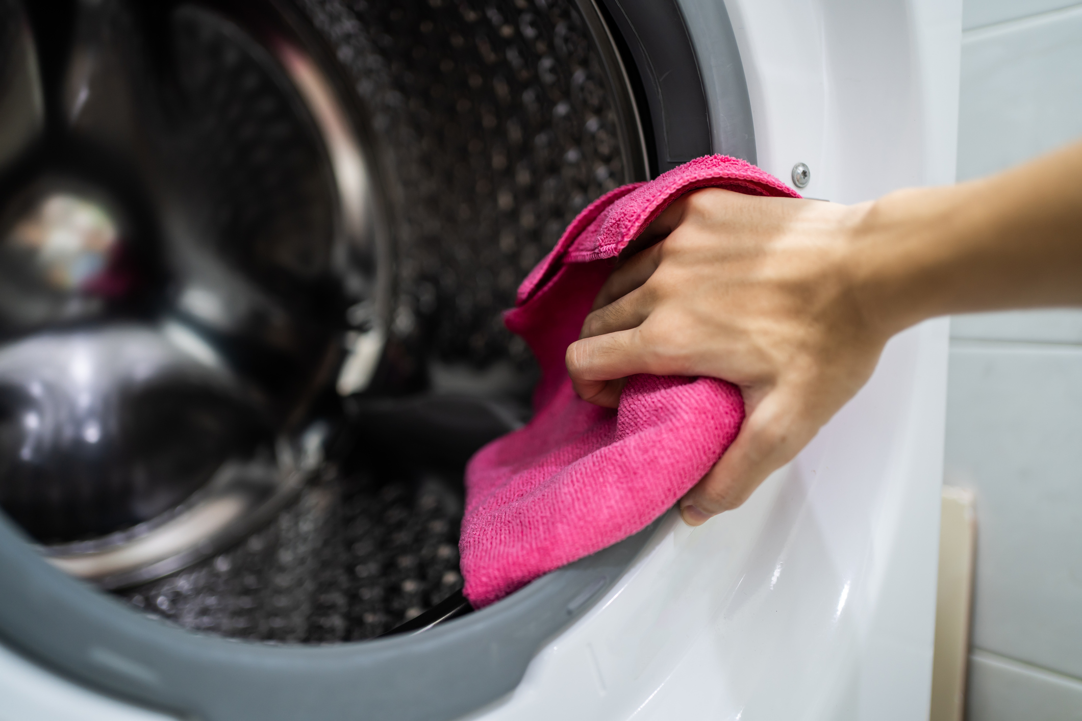A person using a pink cloth to clean a washer gasket 