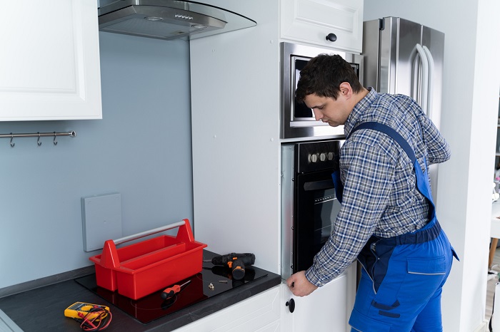 front view of two men installing a wall oven in a modern kitchen