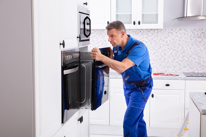 front view of a man installing a wall oven into a modern white kitchen