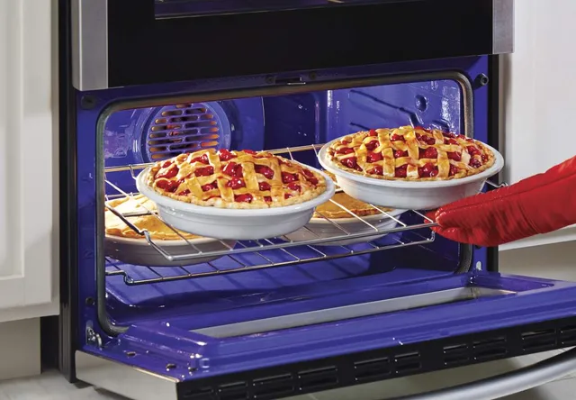 A person inserting two cherry pies on the bottom oven of the LG LDE4413ST double oven range