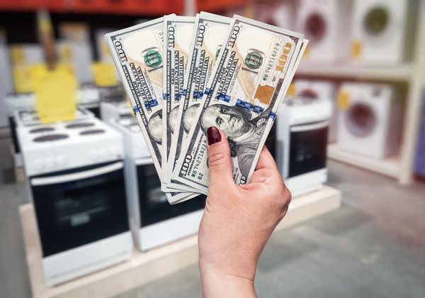 A person holding $100 bills fanned out in front of stoves 