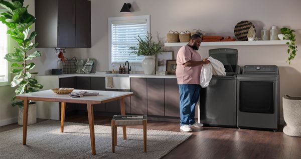 A man in a laundry room pulling a blanket out of a LG top load washer 