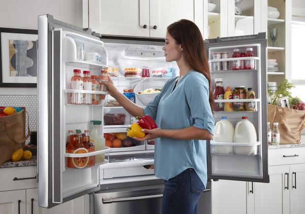 A woman arranging juice bottles inside a Maytag refrigerator 