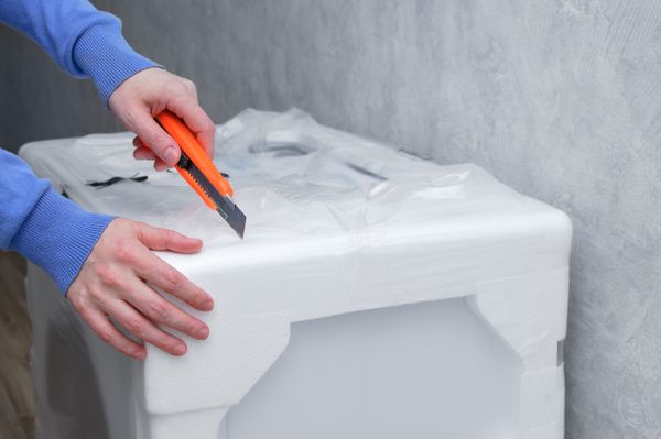A person using a utility knife to open a packaged appliance 