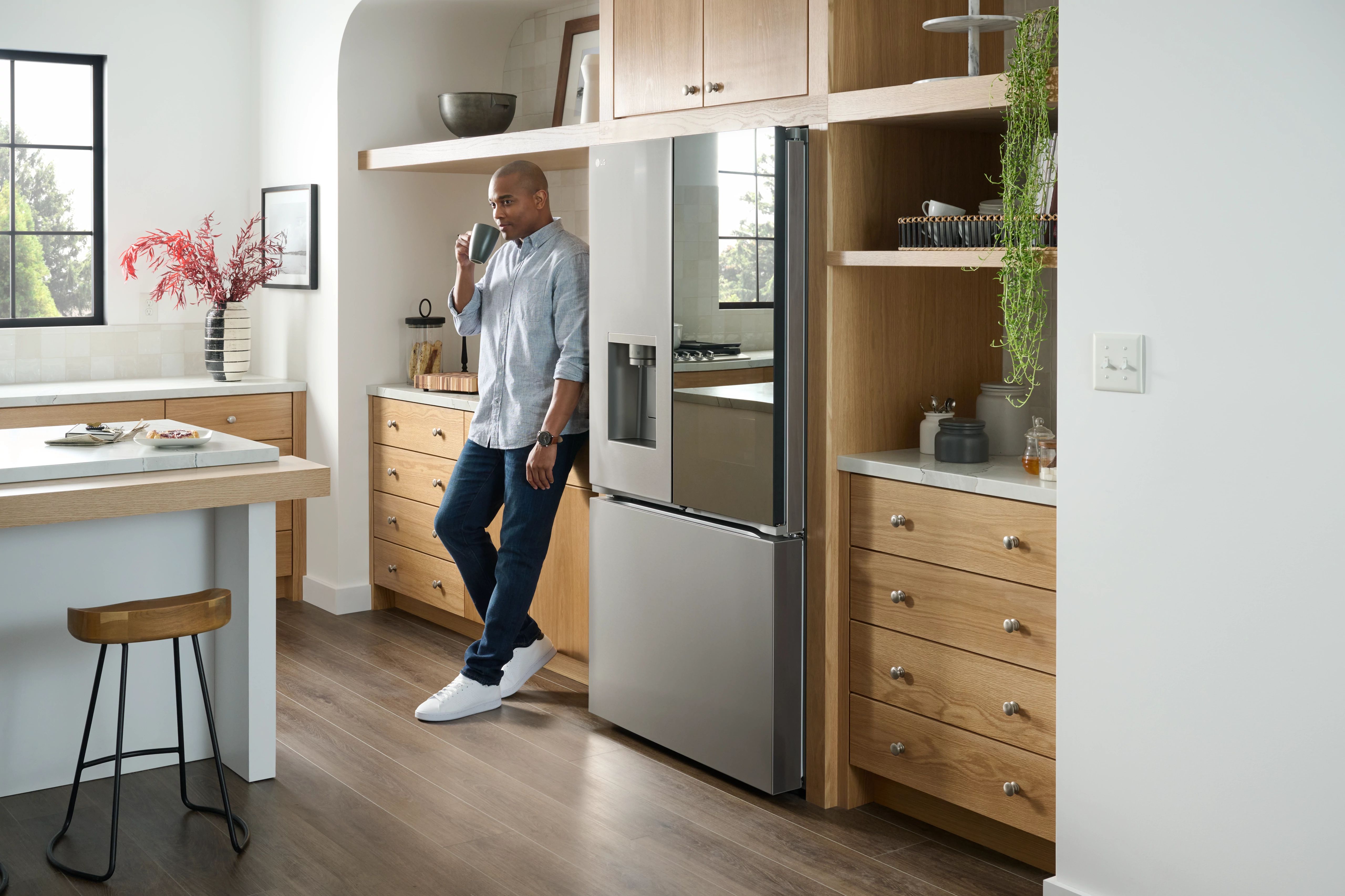 A man enjoying a cup of coffee aside the LG LRYKC2606S InstaView French door refrigerator 