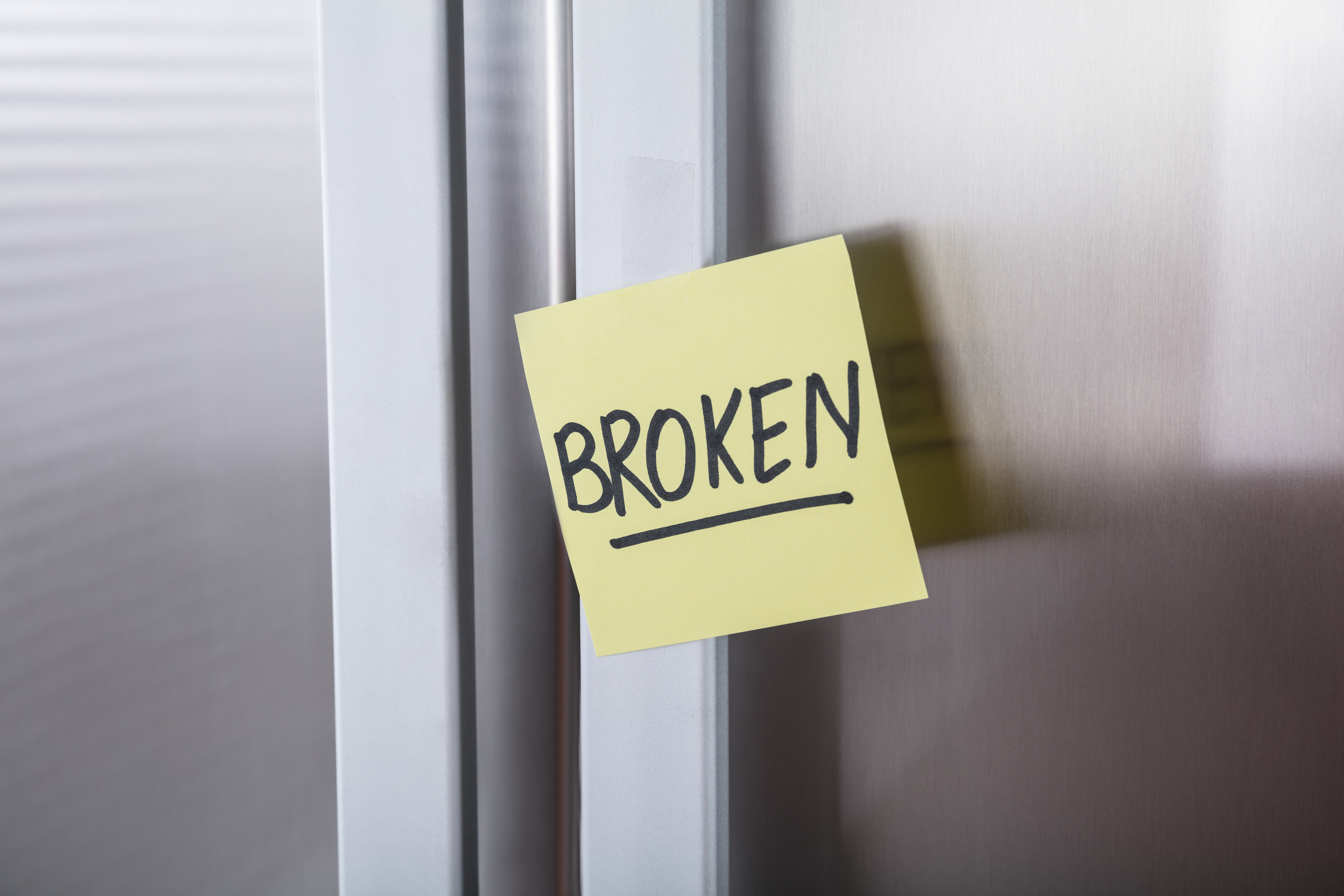 A sticky note saying Broken on a refrigerator door handle 