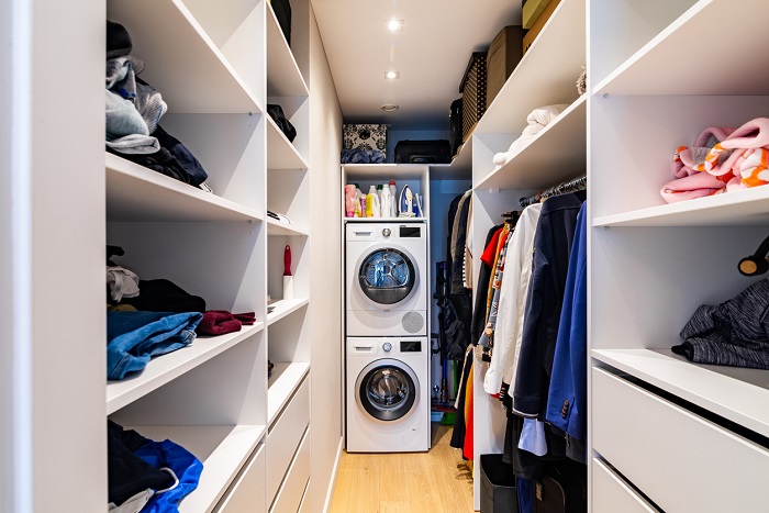 Spacious walk in closet full of clothes with a stacked washer and dryer in the back.