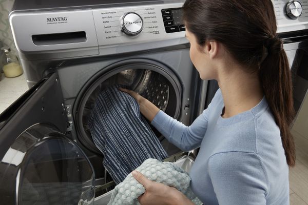 A woman placing items into a Maytag front load washer 