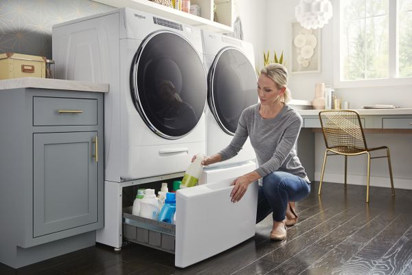 A woman storing items in a pedestal beneath a Whirlpool front load washer and dryer set