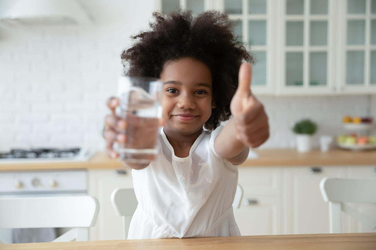 little girl giving a thumbs up and holding a glass of clean drinking water
