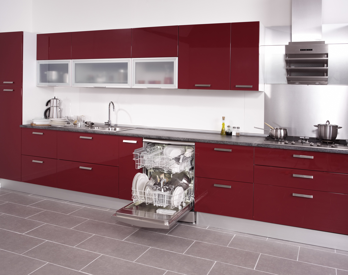 Fully loaded built-in dishwasher with door open against red cabinetry 