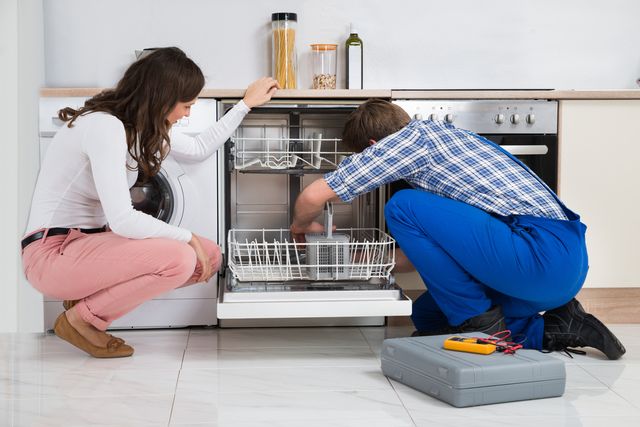 repair man fixing a dishwasher with a woman watching