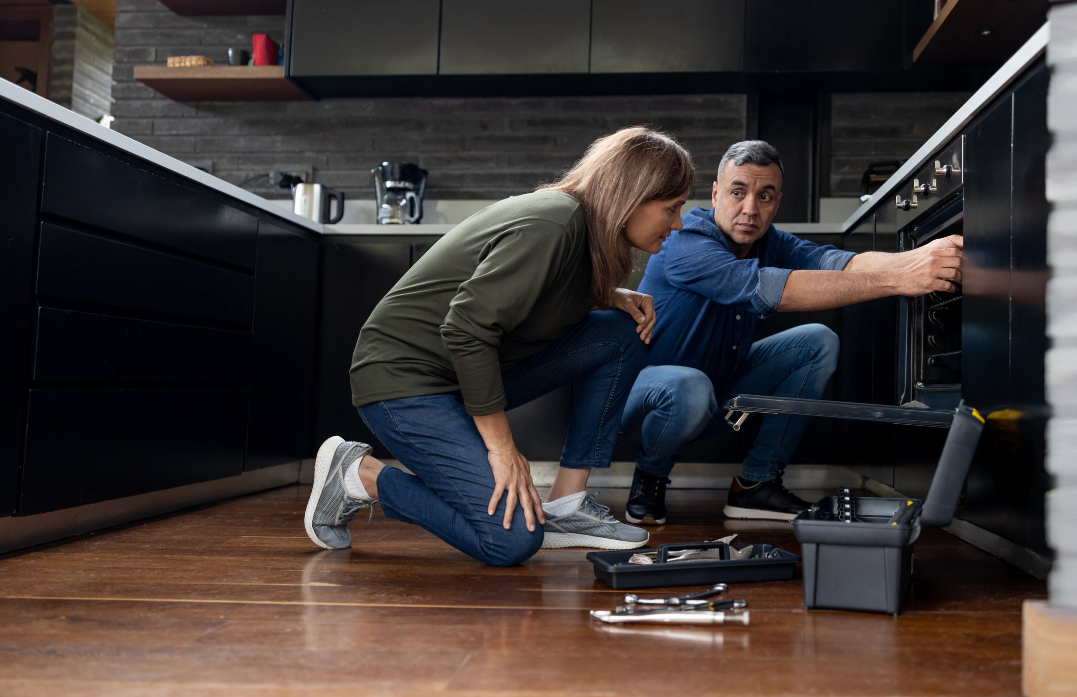 A repair man showing a woman an oven fix 