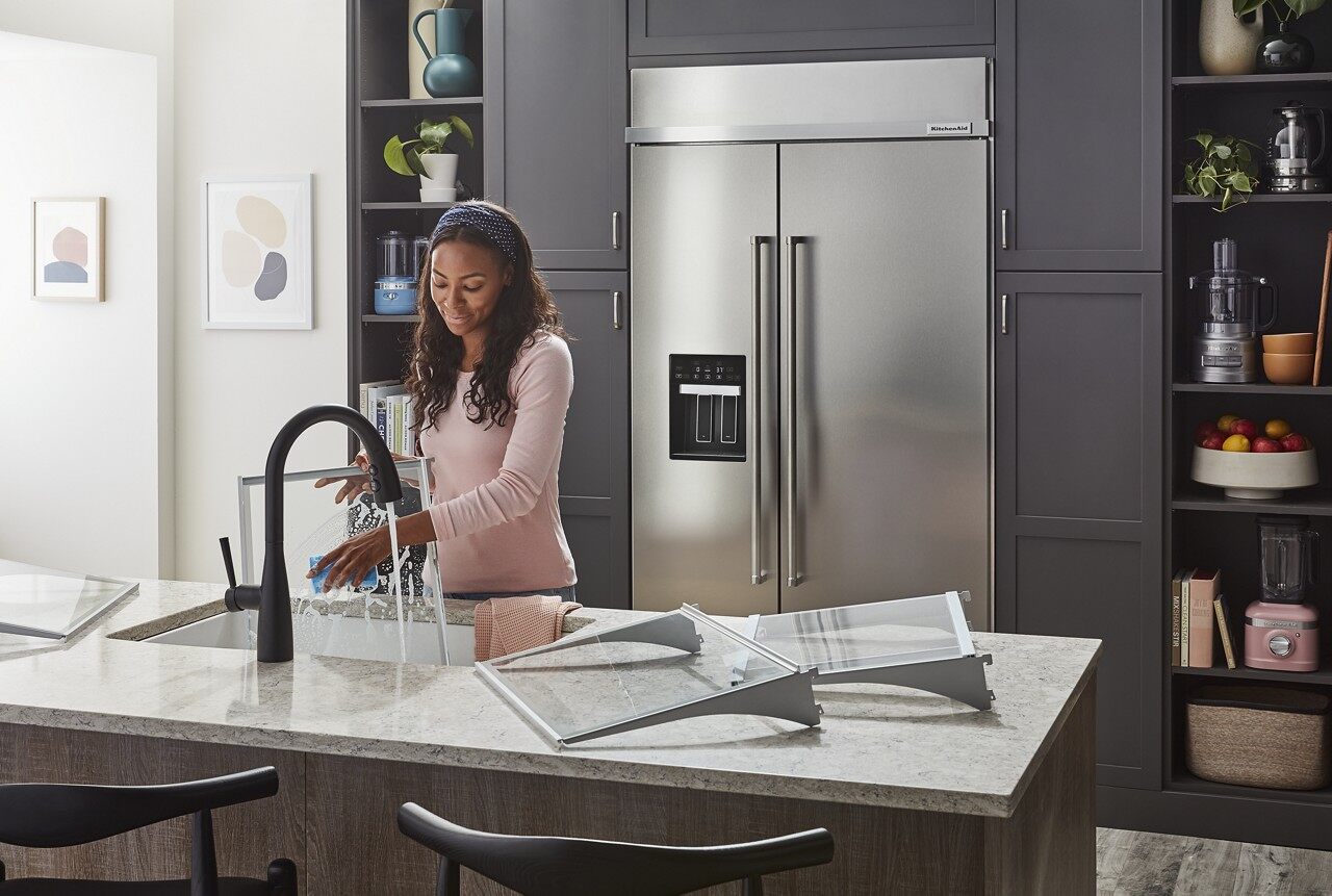 Woman washing dishes with a KitchenAid built in refrigerator in the background 