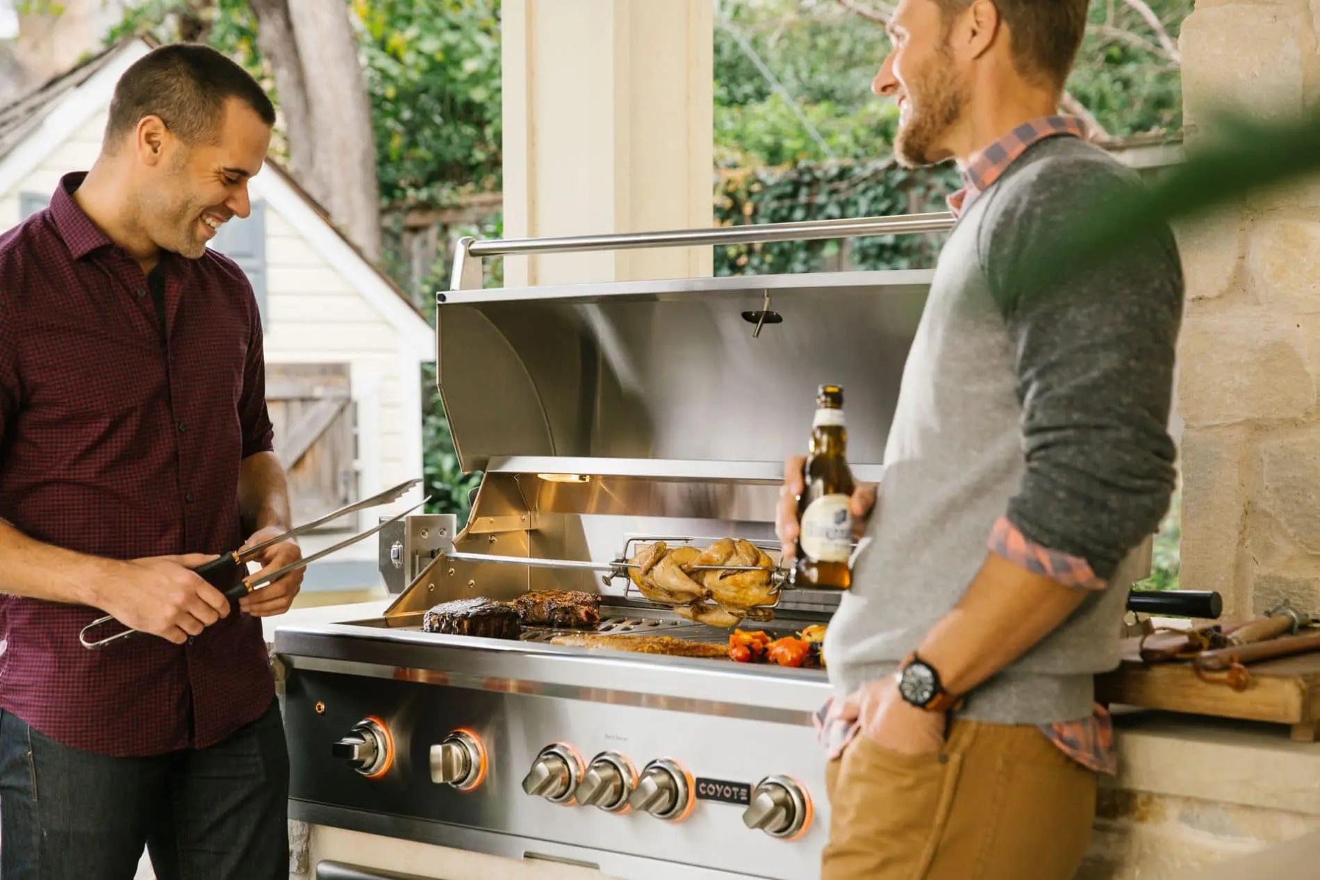 Two men smiling around a Coyote gas grill 