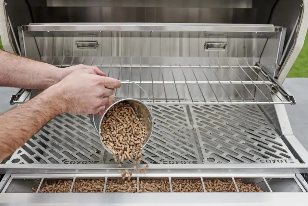 Person loading pellets into a Coyote pellet grill 