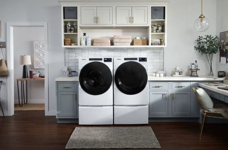 White Whirlpool front load washer with a white Whirlpool dryer in a laundry room with light blue cabinets and dark wood floors
