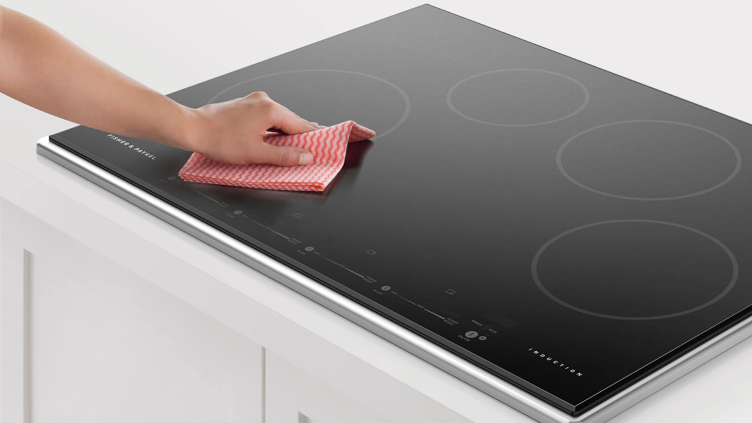 A persons cleaning a Fisher & Paykel induction cooktop with a  cloth 