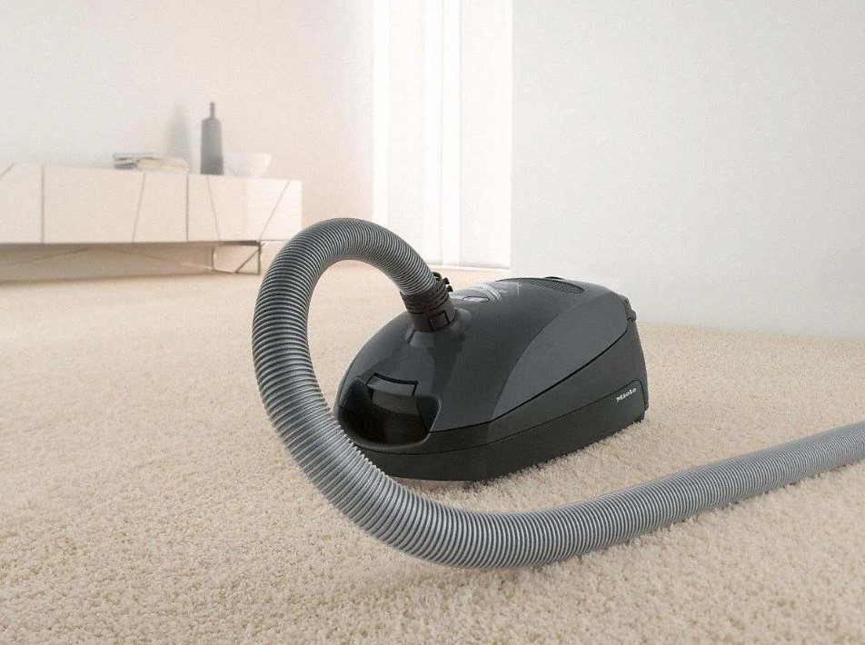 Gray Miele cannister vacuum and hose attachment sitting on a cream colored rug
