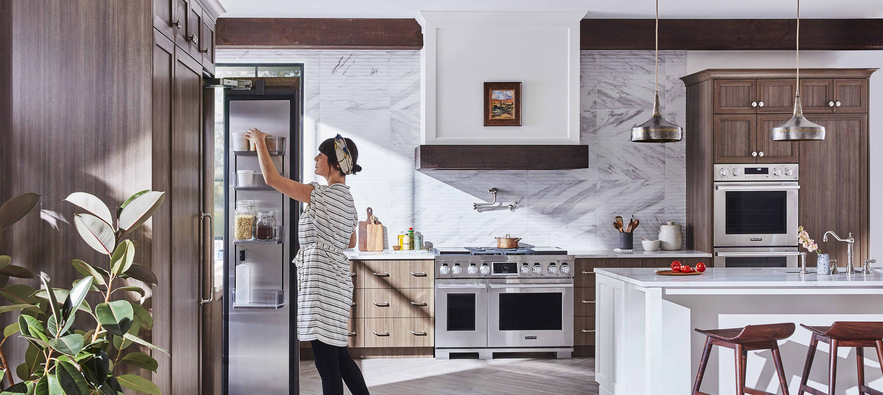 Woman reaches into a refrigerator in a kitchen stocked with luxury appliances
