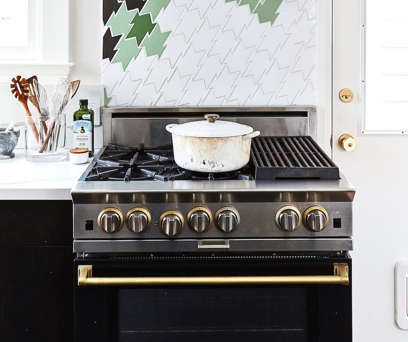 A BlueStar black range with gold hardware against a green and white kitchen backsplash 