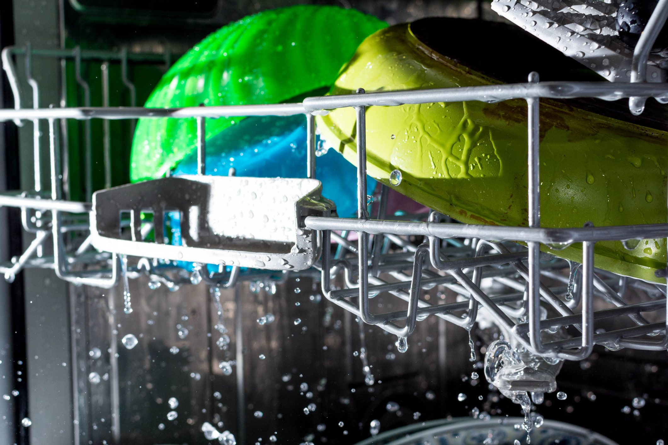 Green and blue plastic dinnerware washing inside a dishwasher 