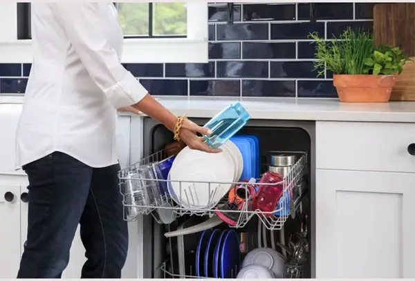 A woman removing a blue sports bottle from the GE GDF450PGRBB black built in dishwasher 