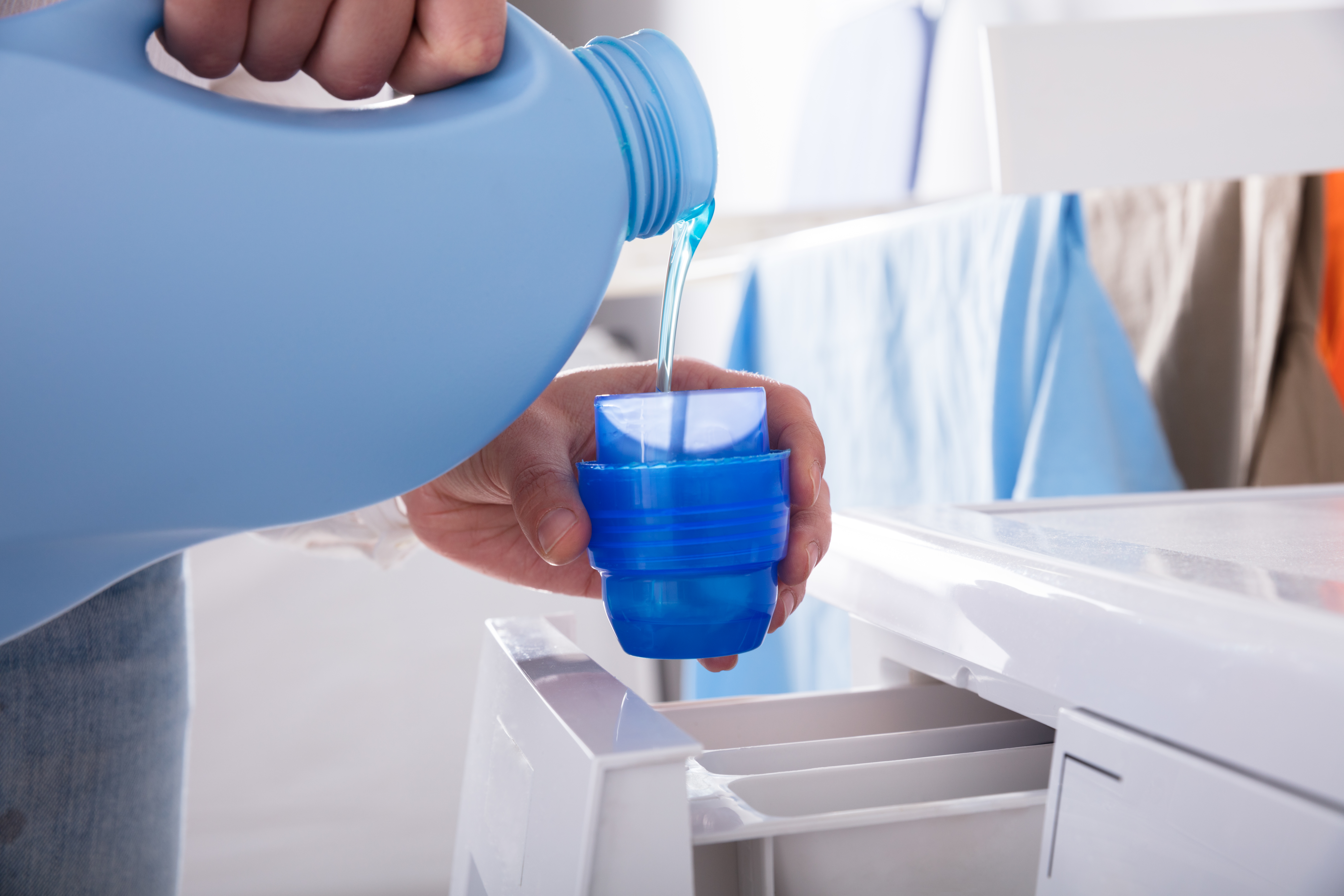 A person pouring liquid detergent into a front load washer 