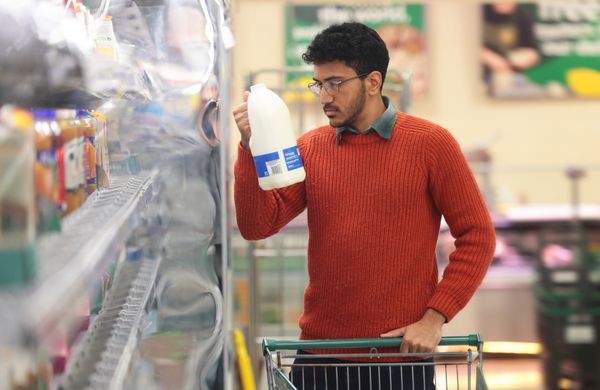 A man in an orange shirt reading a bottle in a grocery store