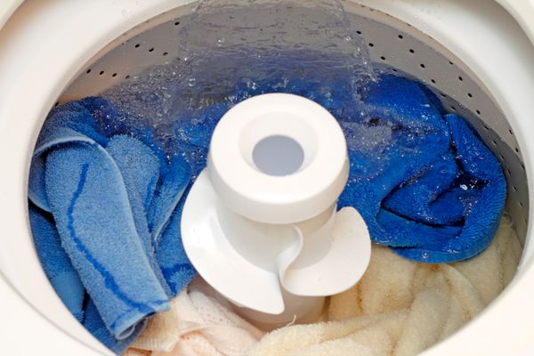A close-up of a top load washer with towels filling with water