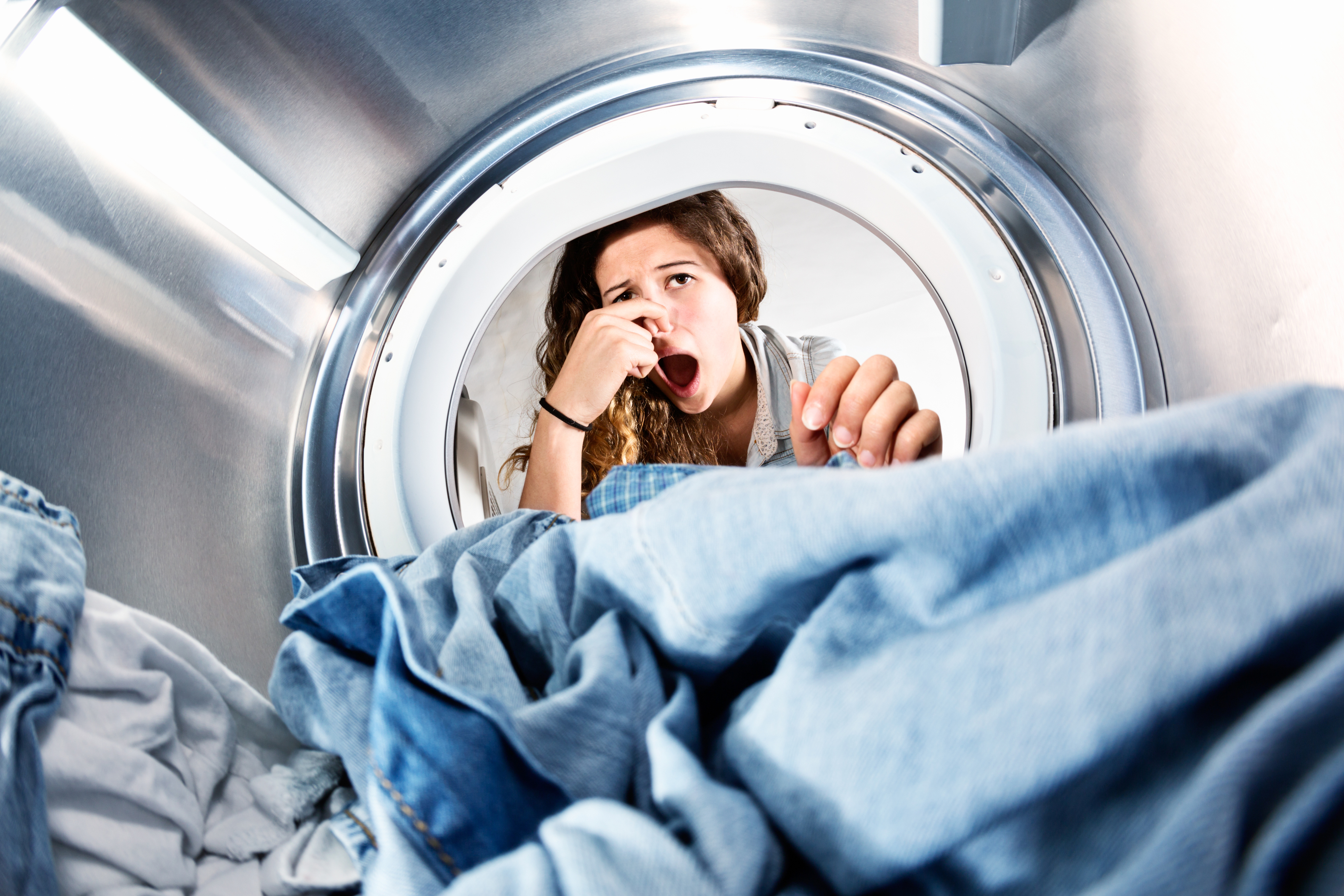 A woman holding her nose while opening the dryer