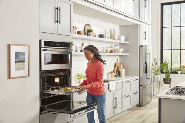 A woman inserting a tray of food into the KitchenAid KOCE900HSS oven 