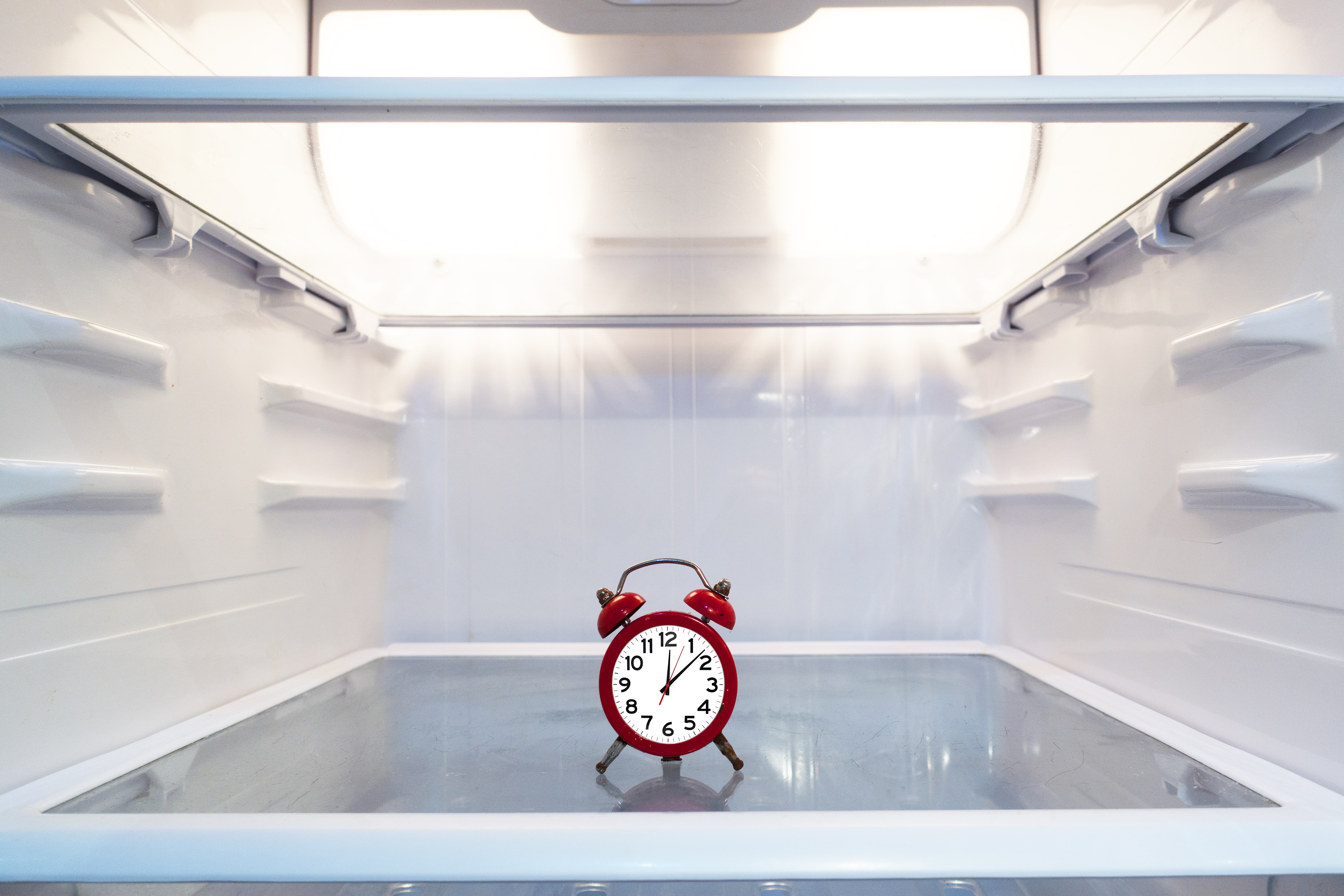 A small, red vintage clock inside of a refrigerator 
